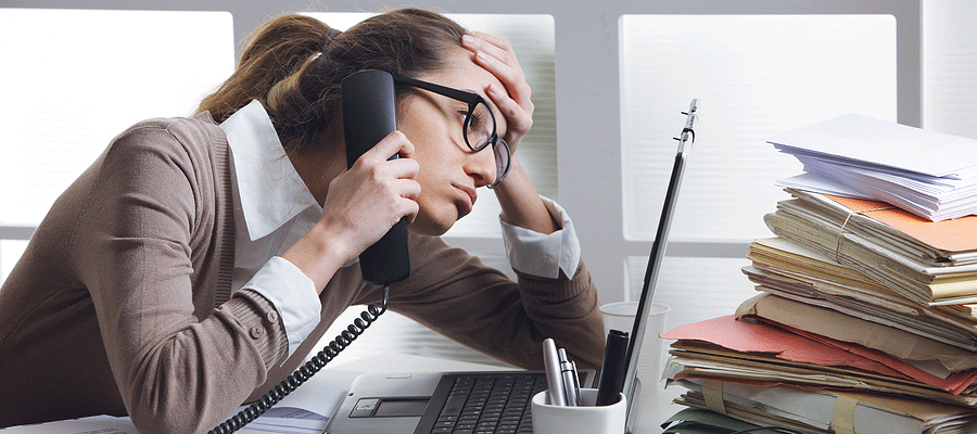 woman sitting at a desk talking on the phone looking stressed