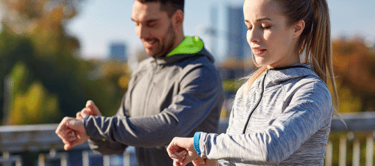 Man and Woman exercising outdoors and looking at their smart watches.